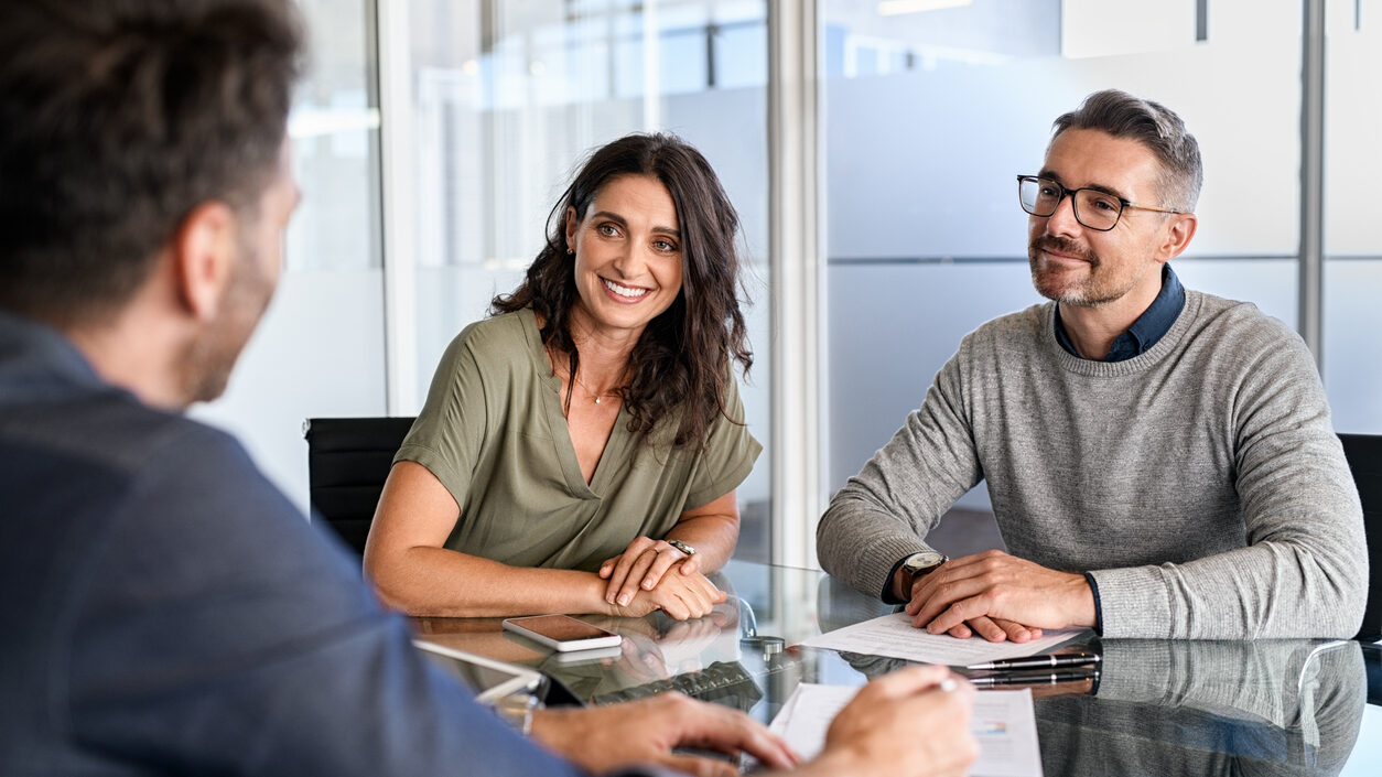 A real estate broker is giving instructions to his affiliated agents inside an office.